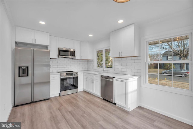 kitchen featuring light wood finished floors, stainless steel appliances, light countertops, and tasteful backsplash