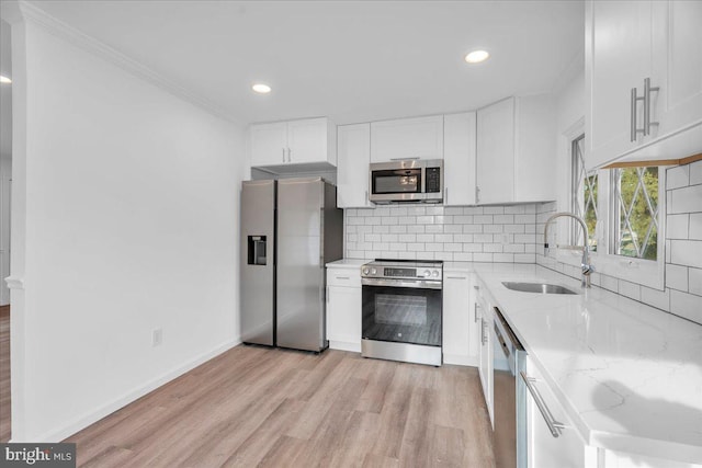 kitchen with a sink, light stone counters, appliances with stainless steel finishes, and white cabinetry