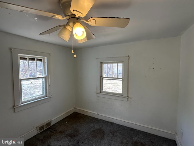 empty room featuring a wealth of natural light, visible vents, baseboards, and dark colored carpet