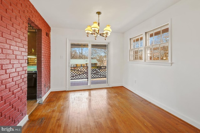 unfurnished dining area featuring hardwood / wood-style floors, an inviting chandelier, baseboards, and brick wall