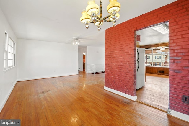 unfurnished living room with visible vents, ceiling fan with notable chandelier, baseboards, and hardwood / wood-style flooring