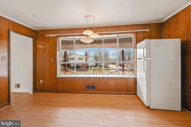 unfurnished dining area with visible vents, light wood-style flooring, wooden walls, and ornamental molding