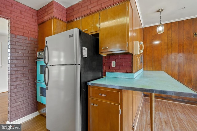 kitchen with double wall oven, brick wall, brown cabinetry, and freestanding refrigerator