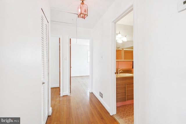 hall featuring a sink, baseboards, attic access, and wood finished floors