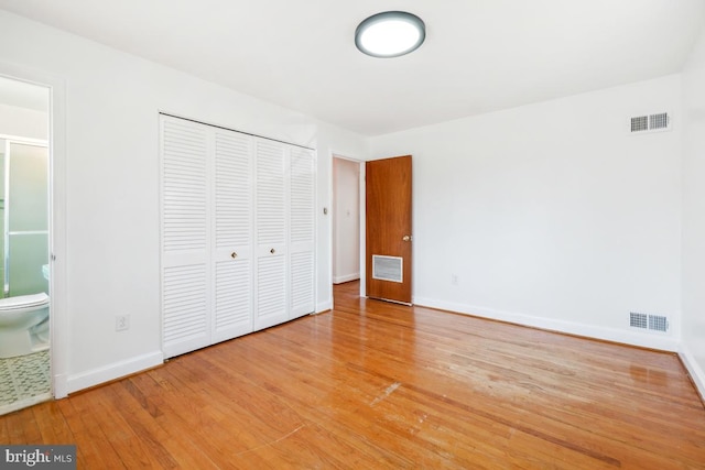 unfurnished bedroom with hardwood / wood-style flooring, baseboards, visible vents, and a closet