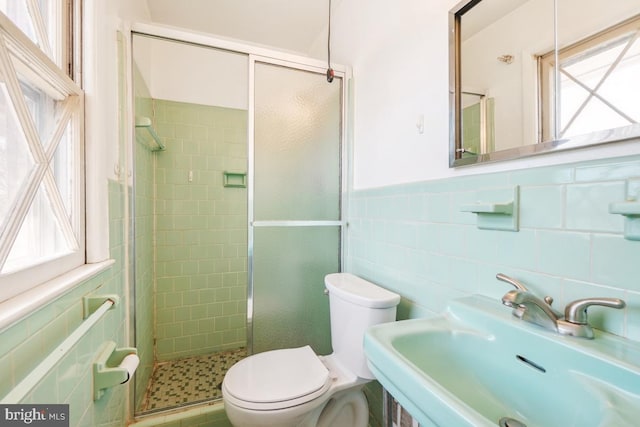 bathroom featuring a wainscoted wall, toilet, a stall shower, tile walls, and a sink