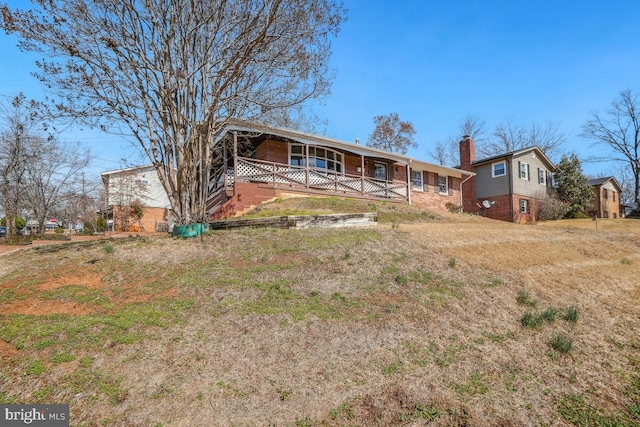 view of front of house with brick siding, a porch, and a chimney