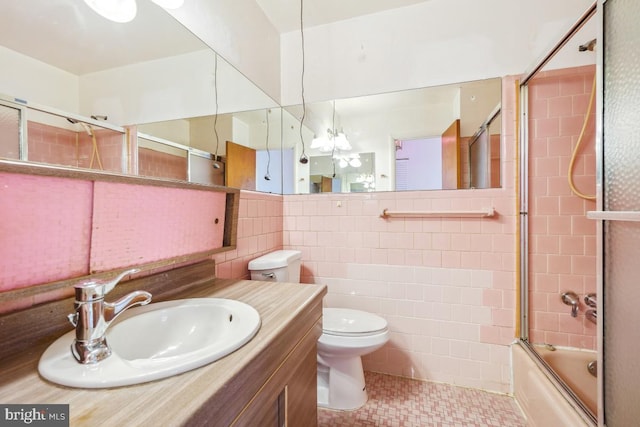 full bath featuring toilet, tile walls, vanity, and shower / bath combination with glass door