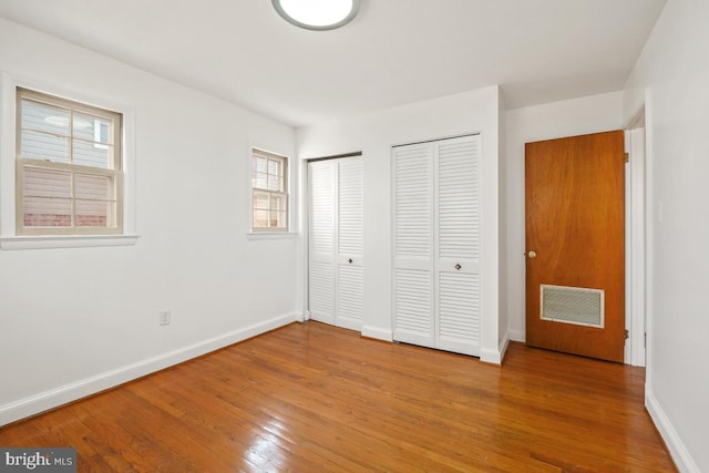 unfurnished bedroom featuring baseboards, visible vents, wood-type flooring, and multiple closets