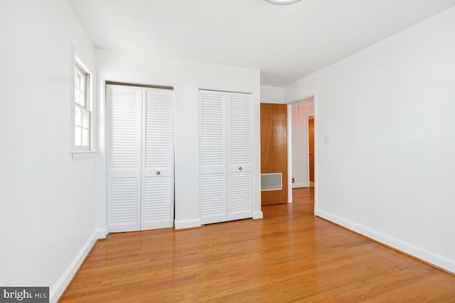 unfurnished bedroom featuring visible vents, baseboards, light wood-style floors, and multiple closets