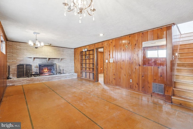 unfurnished living room featuring built in features, visible vents, an inviting chandelier, wood walls, and a brick fireplace