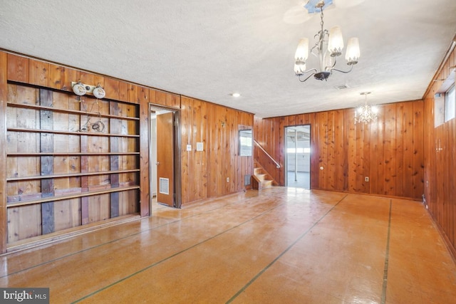 hallway with a textured ceiling, finished concrete floors, wooden walls, an inviting chandelier, and stairs