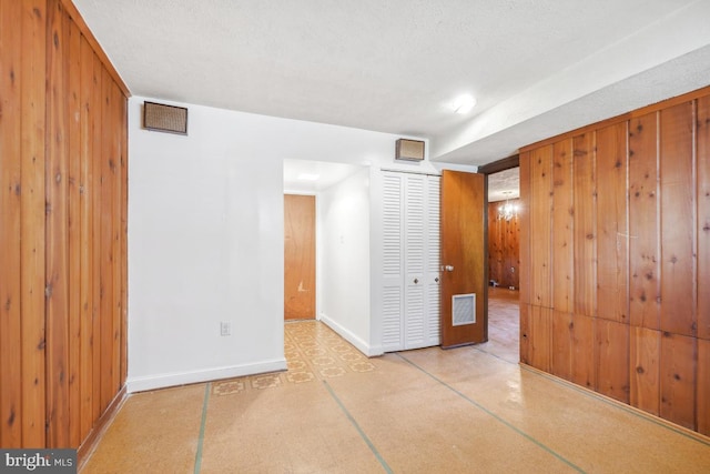 unfurnished room featuring visible vents, wood walls, a textured ceiling, and baseboards