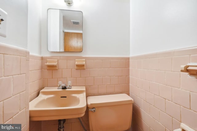 half bath featuring visible vents, toilet, a wainscoted wall, and a sink