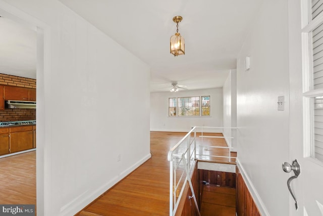 hallway with an upstairs landing, baseboards, and light wood finished floors