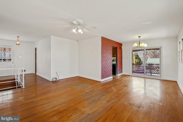 unfurnished living room featuring hardwood / wood-style flooring, a brick fireplace, ceiling fan with notable chandelier, and baseboards