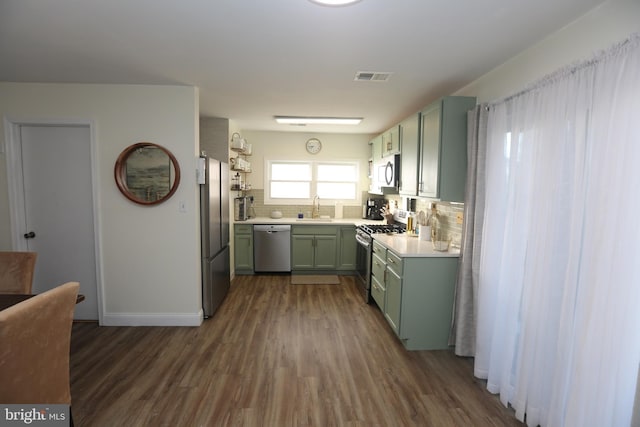 kitchen with visible vents, green cabinets, decorative backsplash, appliances with stainless steel finishes, and a sink