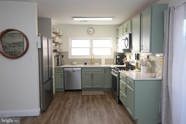 kitchen featuring light countertops, decorative backsplash, dark wood-style floors, stainless steel appliances, and a sink