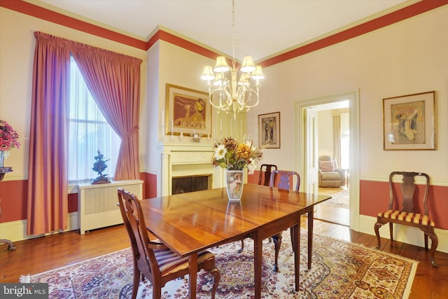 dining area with wood-type flooring, radiator, a fireplace, crown molding, and a chandelier