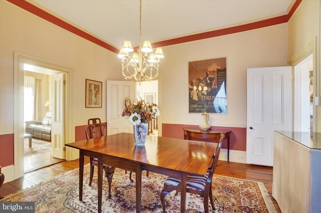 dining space featuring baseboards, wood finished floors, an inviting chandelier, and ornamental molding