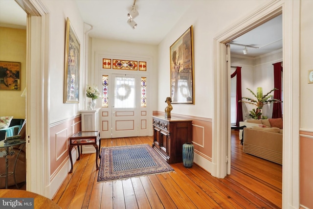 entryway featuring light wood-type flooring, a wainscoted wall, rail lighting, and a decorative wall