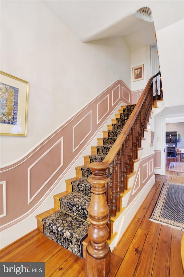 stairway with wood-type flooring, wainscoting, and a decorative wall