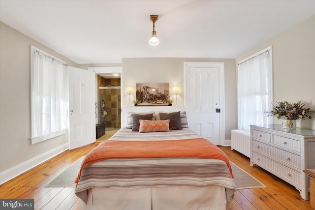 bedroom with radiator heating unit, light wood-type flooring, and baseboards