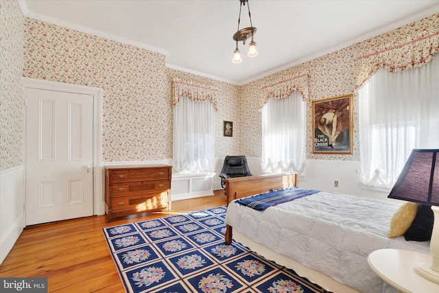 bedroom with wallpapered walls, wood finished floors, a wainscoted wall, and ornamental molding