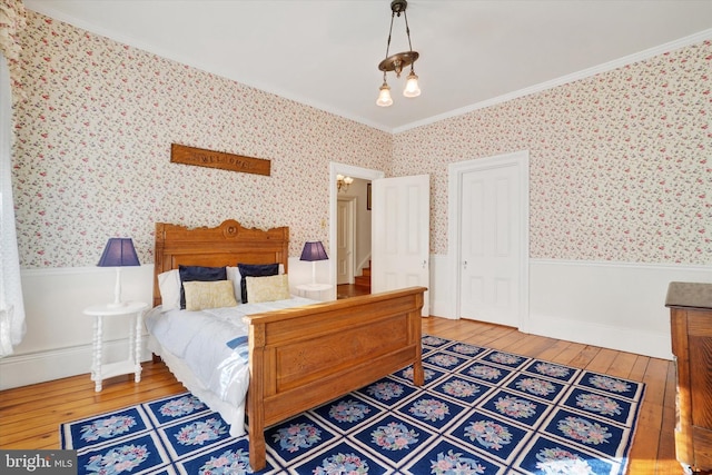 bedroom featuring a wainscoted wall, hardwood / wood-style flooring, ornamental molding, and wallpapered walls