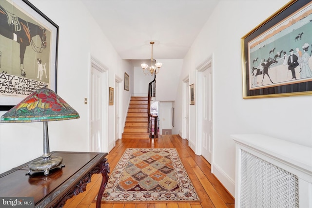 corridor featuring light wood-style flooring, radiator, an inviting chandelier, baseboards, and stairs