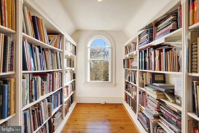 unfurnished room featuring bookshelves, lofted ceiling, and hardwood / wood-style floors