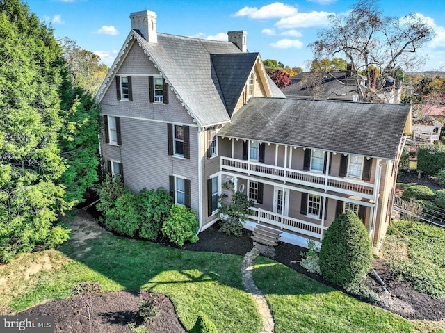 exterior space with a front lawn, a balcony, covered porch, and a chimney