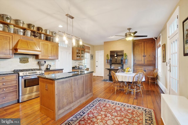 kitchen featuring premium range hood, a sink, hardwood / wood-style floors, gas stove, and dark stone counters