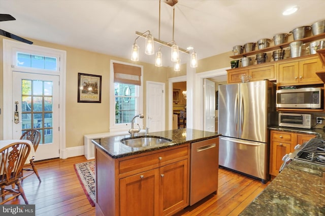 kitchen with brown cabinets, a sink, dark stone countertops, stainless steel appliances, and light wood finished floors