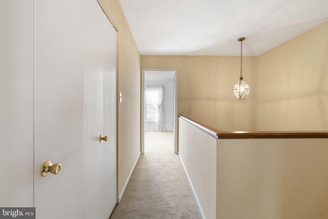 hallway with baseboards, light carpet, and an upstairs landing