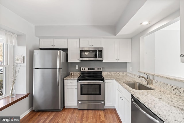 kitchen featuring a sink, white cabinetry, stainless steel appliances, light wood finished floors, and light stone countertops