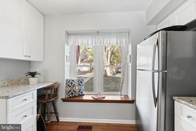 kitchen with wood finished floors, visible vents, baseboards, freestanding refrigerator, and white cabinetry