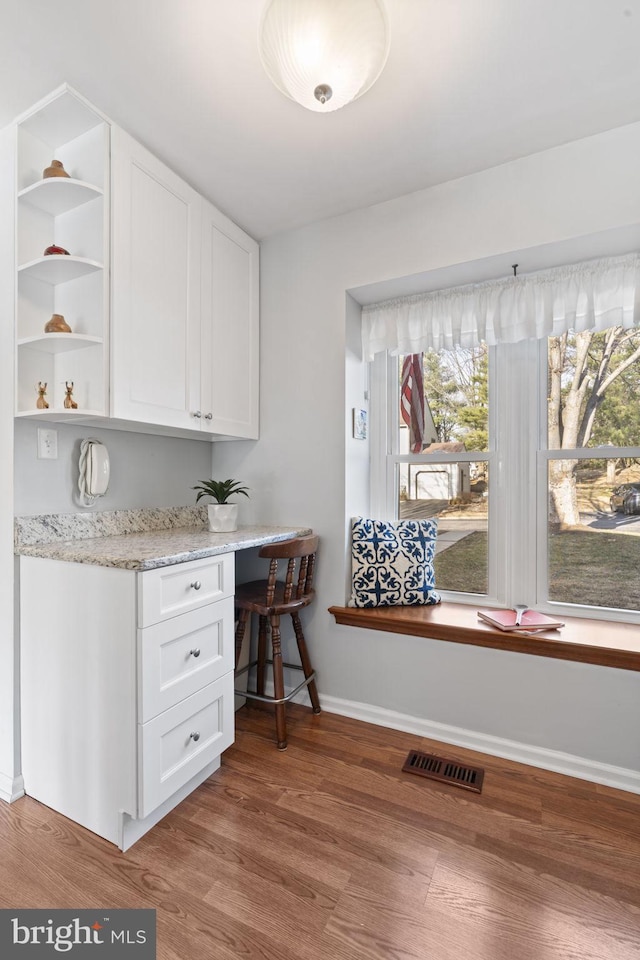 interior space with visible vents, baseboards, wood finished floors, and built in desk