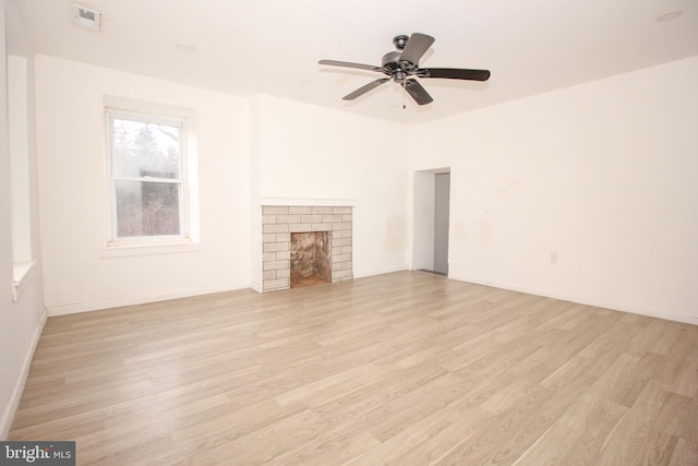 unfurnished living room with baseboards, a brick fireplace, a ceiling fan, and light wood-style floors