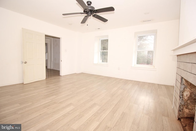 unfurnished living room featuring a wealth of natural light, a ceiling fan, a tiled fireplace, and light wood finished floors