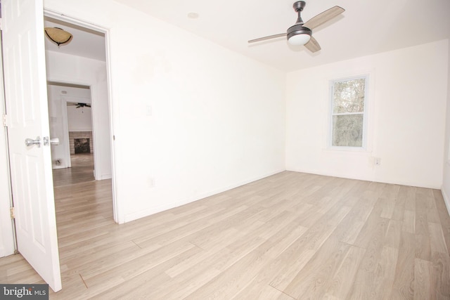 empty room with light wood finished floors, a brick fireplace, baseboards, and ceiling fan