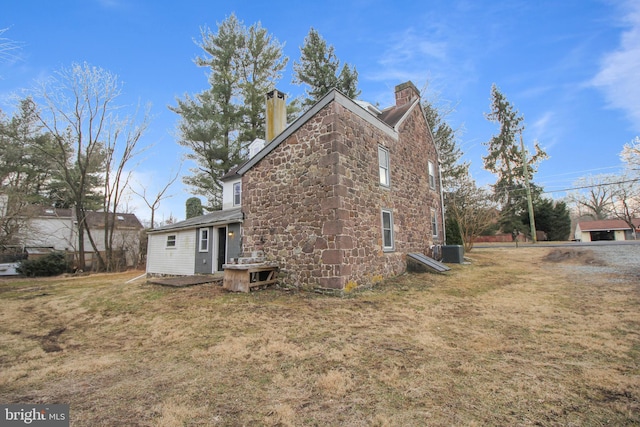 view of side of home with cooling unit, a lawn, stone siding, and a chimney