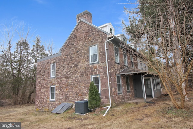 view of side of property featuring stone siding, central AC, and a chimney