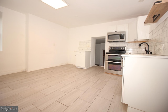 kitchen featuring a sink, tasteful backsplash, white cabinetry, stainless steel appliances, and light countertops