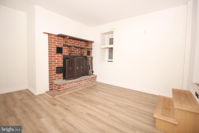 unfurnished living room with a brick fireplace, wood finished floors, and baseboards