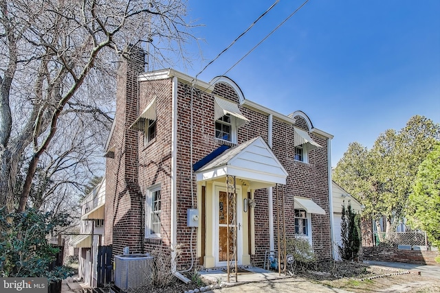 view of front of home featuring brick siding, central air condition unit, and a chimney