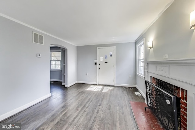 unfurnished living room featuring visible vents, baseboards, a fireplace with flush hearth, wood finished floors, and arched walkways