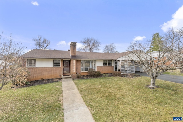 ranch-style home with aphalt driveway, a front yard, brick siding, and a chimney