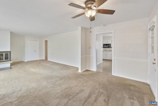 unfurnished living room with a glass covered fireplace, carpet flooring, a ceiling fan, and baseboards