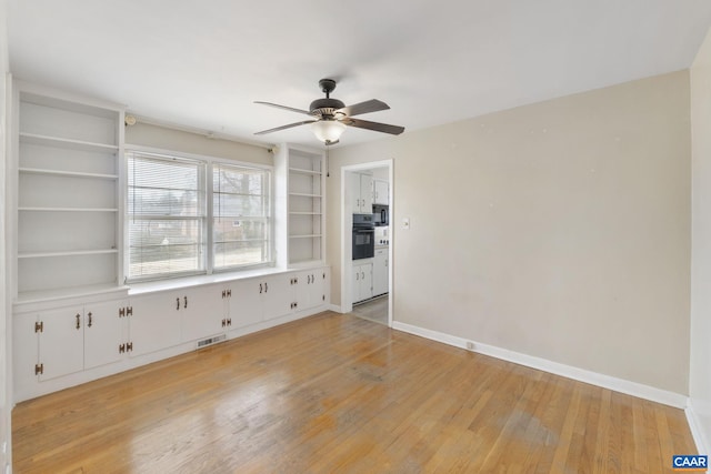 spare room with ceiling fan, visible vents, light wood-type flooring, and baseboards